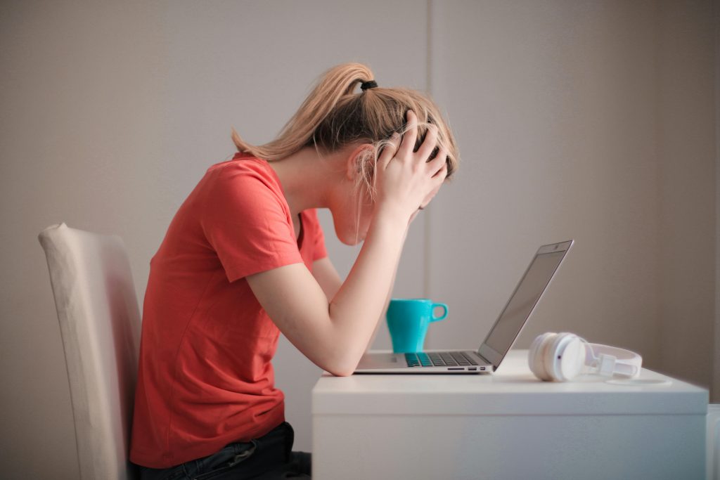 Stressed person at laptop with head in hands.