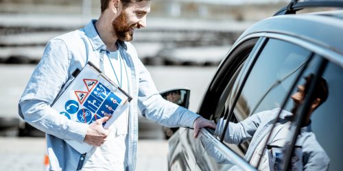 Driving instructor holding clipboard beside car