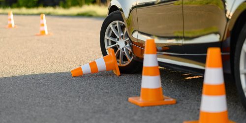 Car tire near orange traffic cones on road.
