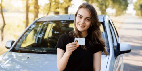 Smiling person holding driver's license by car